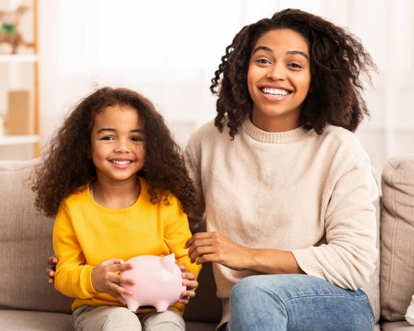 Personal Savings. Happy Mother And Daughter Holding Piggybank Embracing Sitting On Sofa At Home